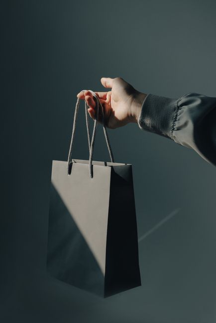 A minimalistic photo of a hand holding a gray shopping bag against a studio background.