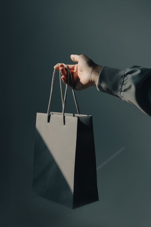 Free A minimalistic photo of a hand holding a gray shopping bag against a studio background. Stock Photo