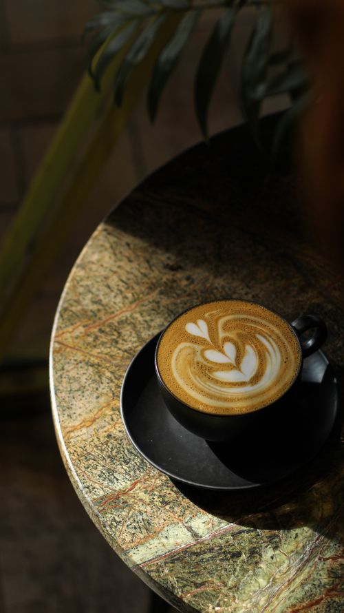 Free A beautifully crafted latte with intricate art served in a sunlit cafe setting, perfect for coffee lovers. Stock Photo