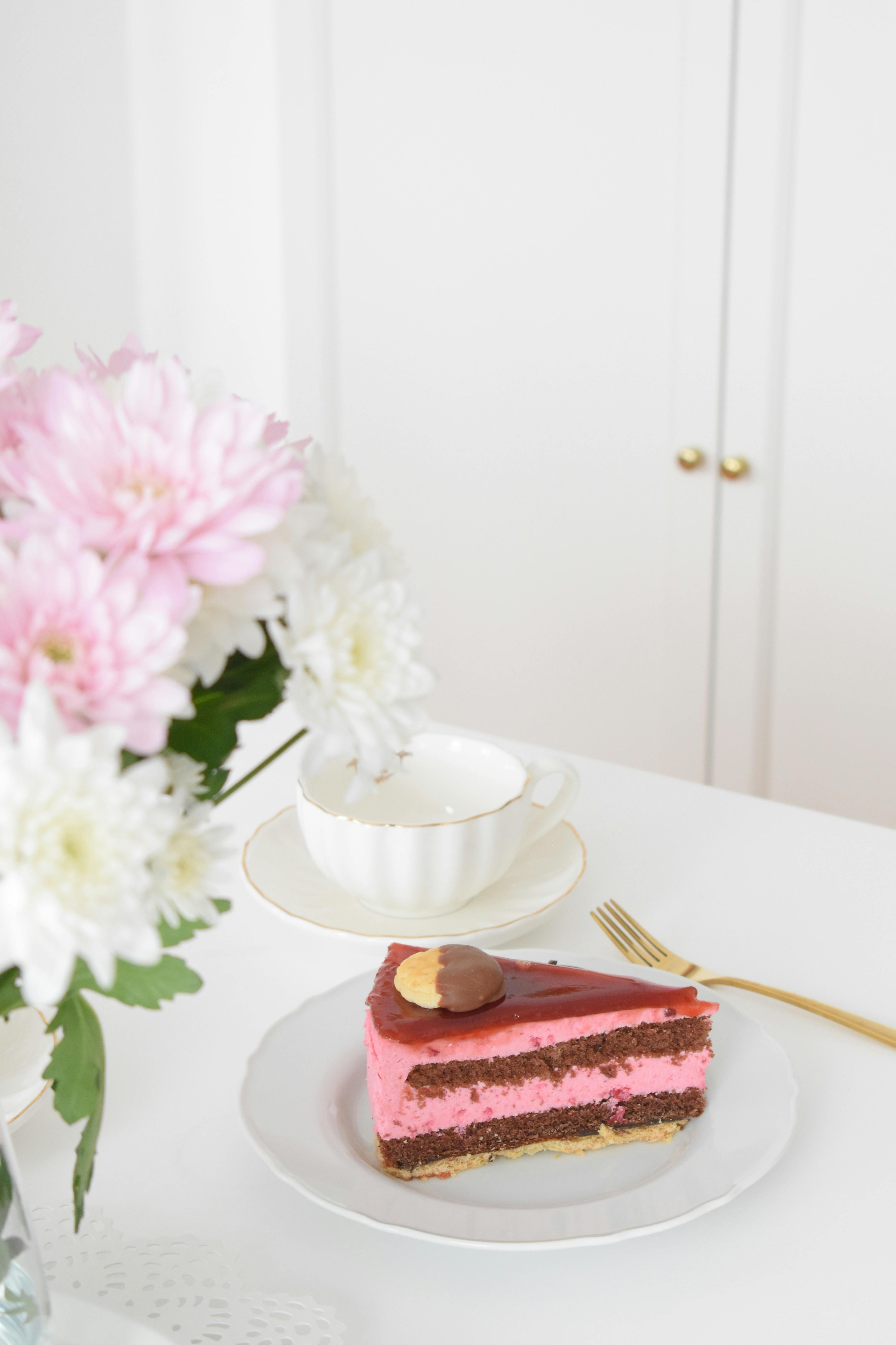 Slice of pink dessert cake on a plate with floral arrangement. Perfect for upscale dining scenes.