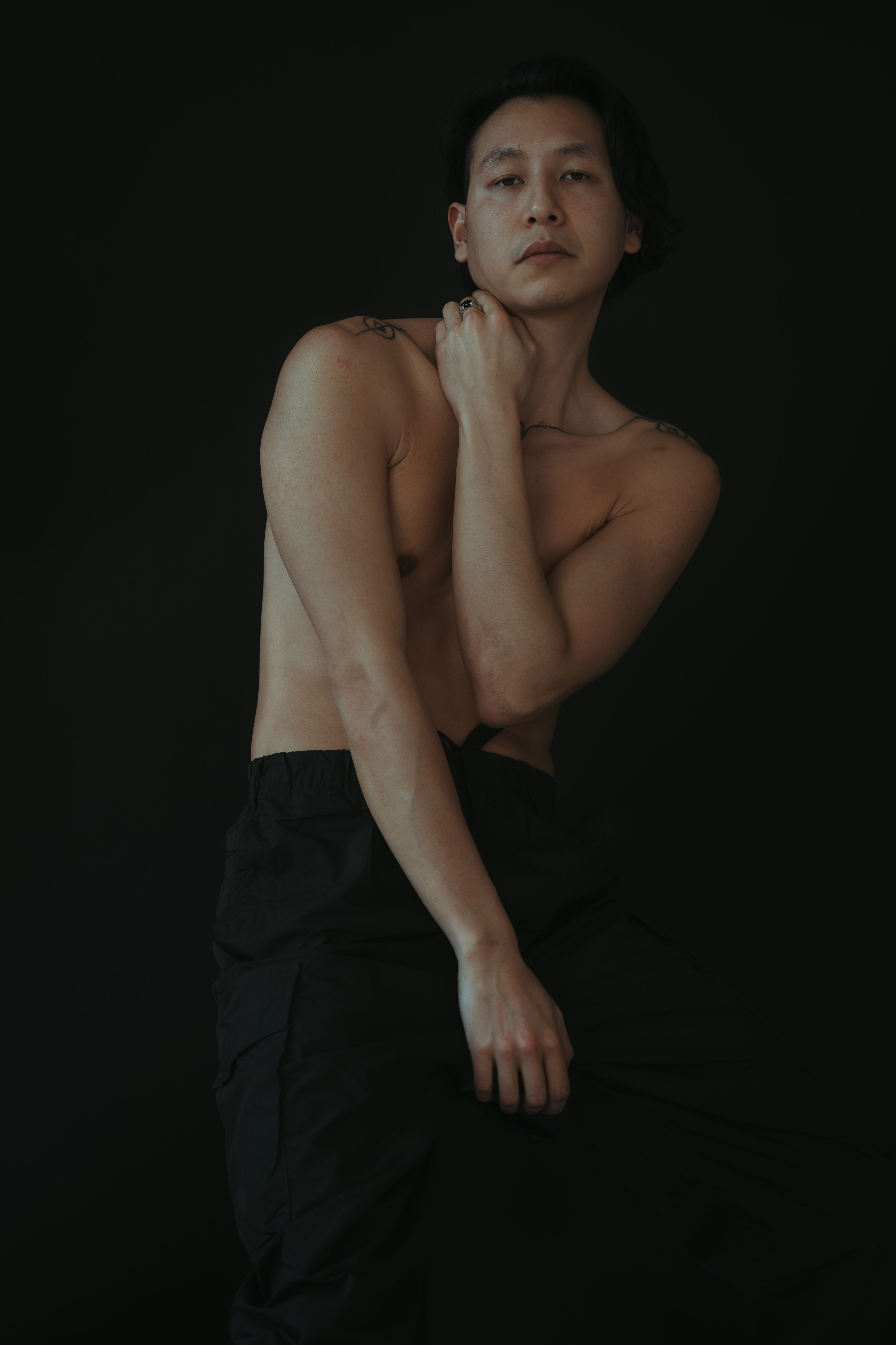Artistic studio portrait of a topless man with a dark background, showcasing modern style.