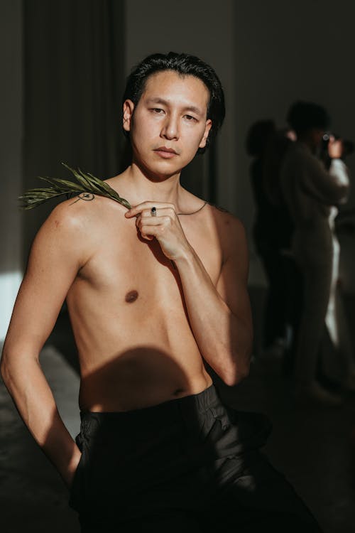 A Shirtless Man Posing in Sunlight while Holding a Palm Leaf 