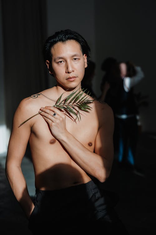 A shirtless man holding a plant in his hand