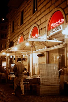 Cozy Italian pizzeria with outdoor dining under umbrellas on a bustling city night.