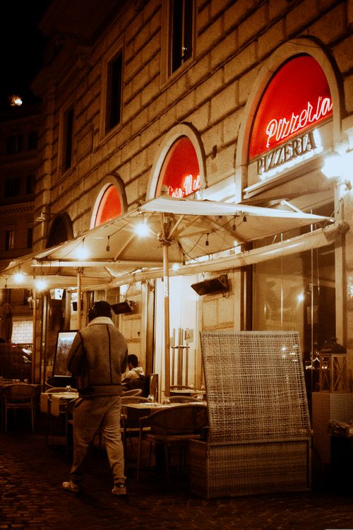 Free Cozy Italian pizzeria with outdoor dining under umbrellas on a bustling city night. Stock Photo
