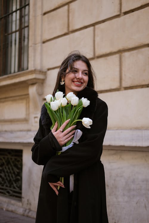 Young Woman with a Bunch of White Tulips Standing on a Sidewalk 