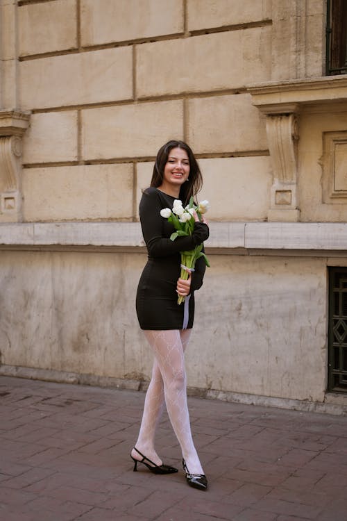 Elegant Woman with a Bunch of White Tulips Standing on a Sidewalk 