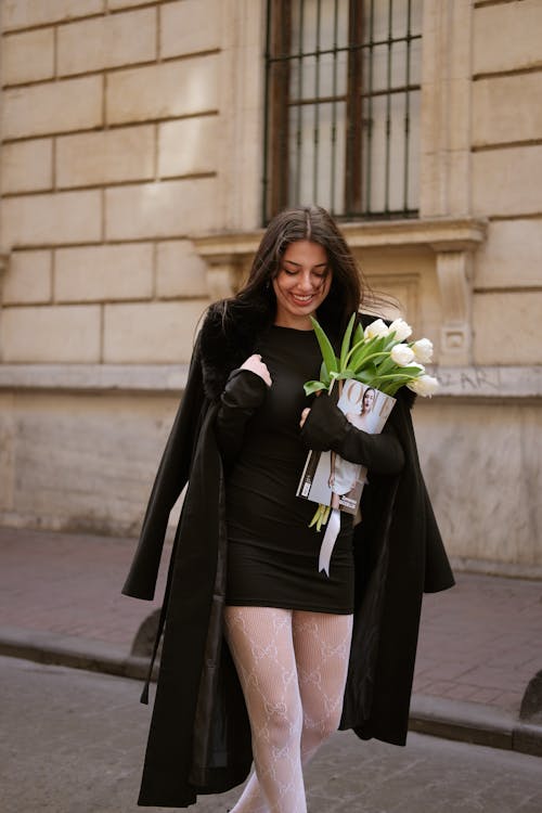 A woman in a black coat and white stockings holding a bouquet of flowers