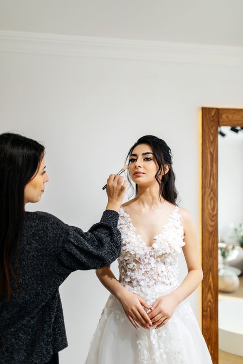 Free A bride in a beautiful gown being prepared by a beautician with elegant makeup indoors. Stock Photo