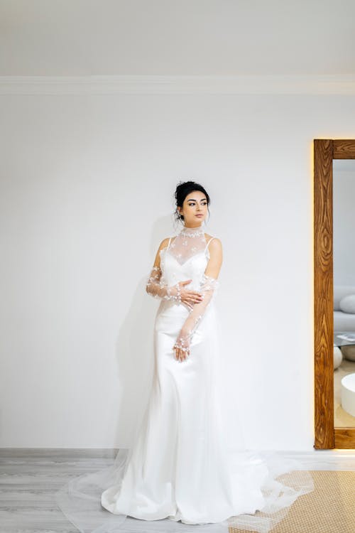 A woman in a wedding dress stands in front of a mirror