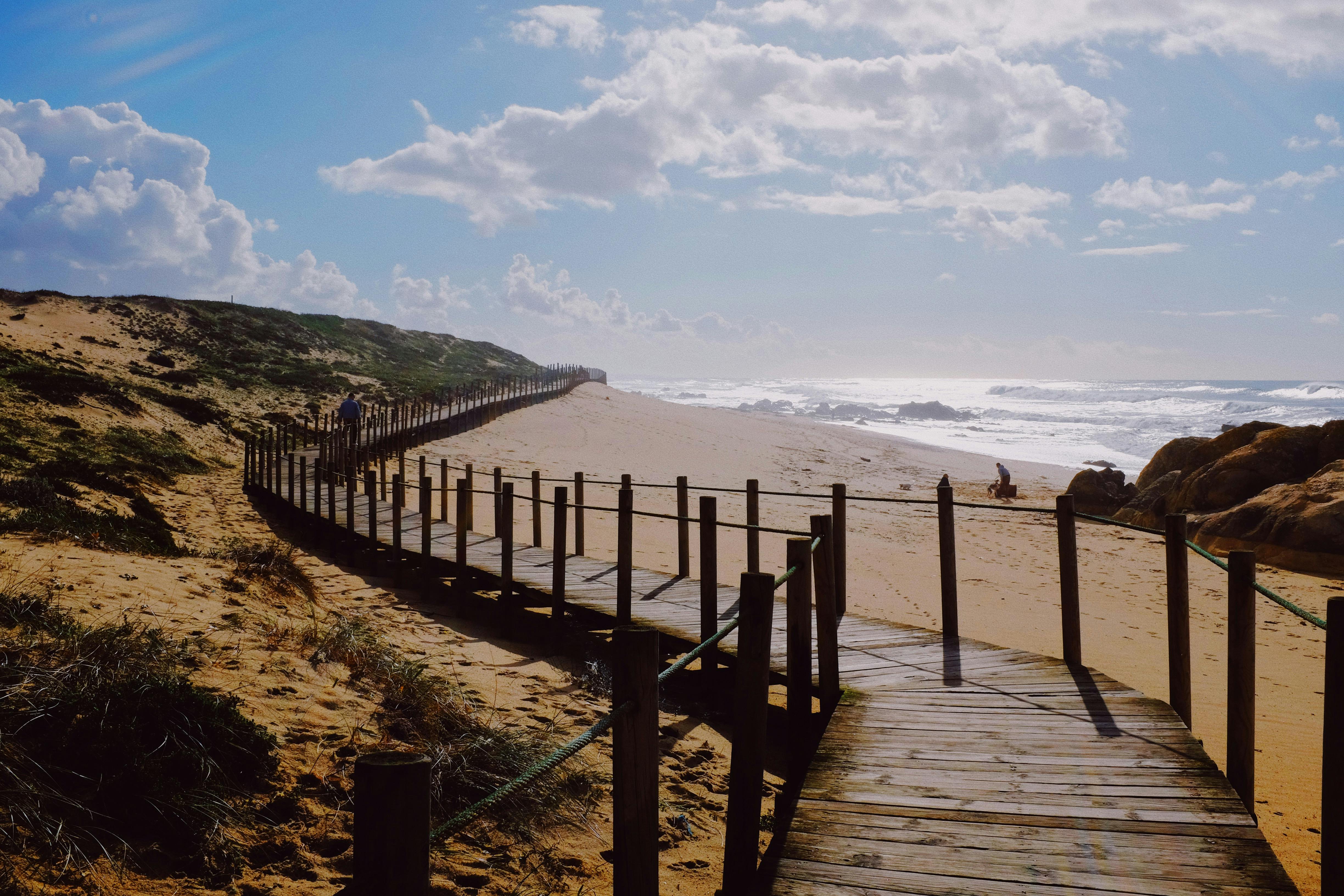 Wooden walkway and sandy beach under bright sunlight in Porto, Portugal.