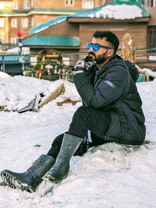 A man sitting on the snow wearing sunglasses