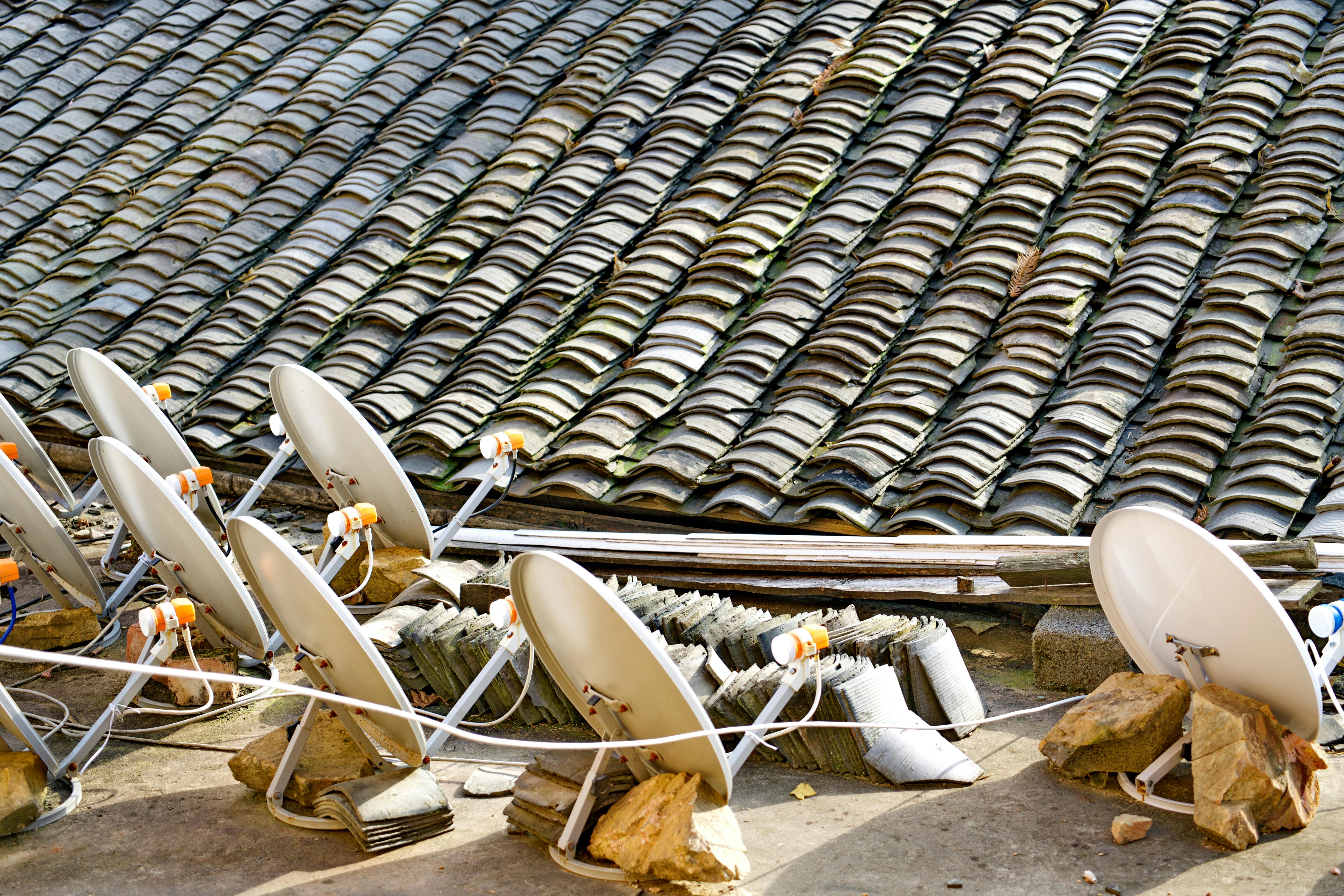 A row of satellite dishes set against an intricately tiled roof, depicting modern technology blending with traditional architecture.