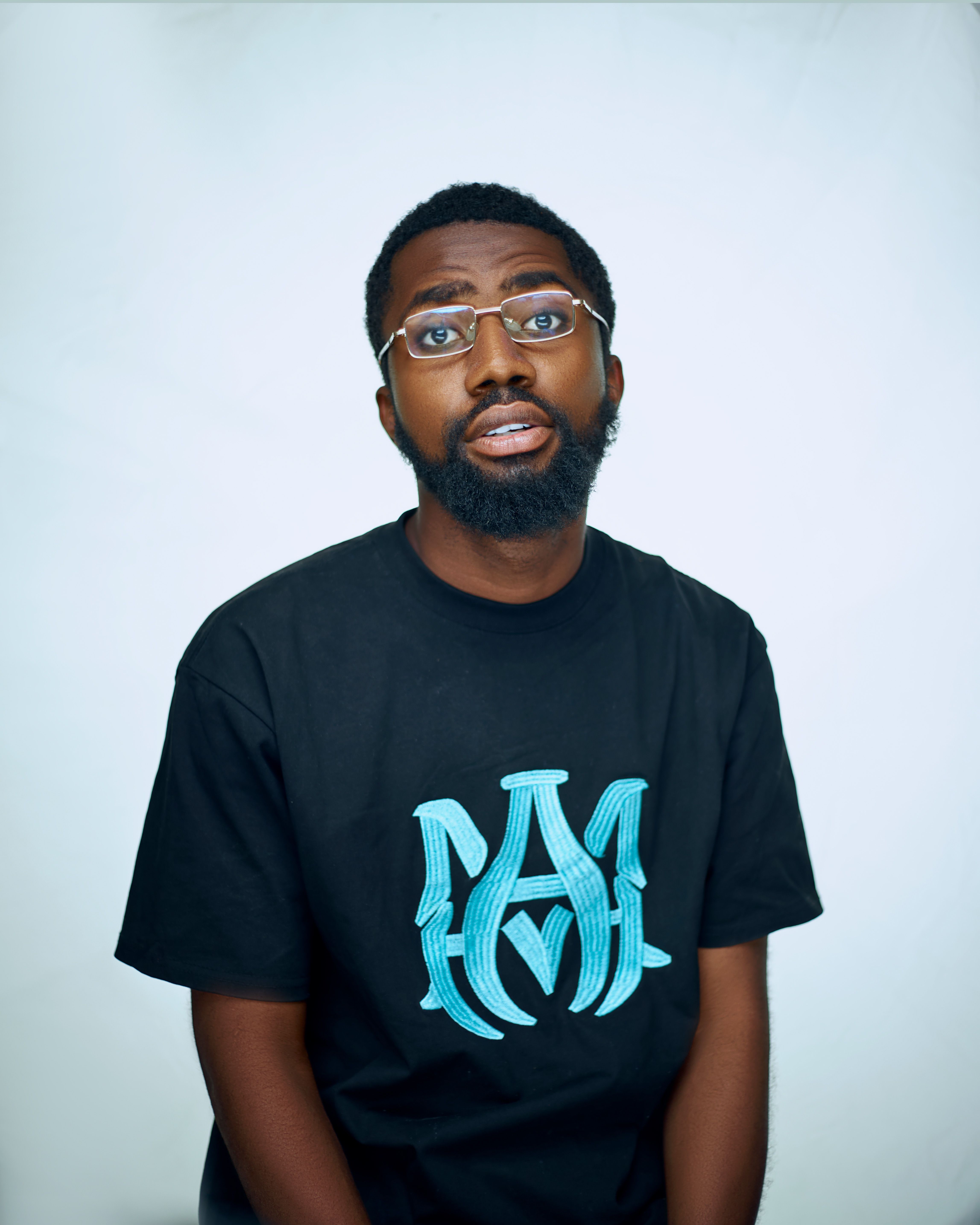 Portrait of a fashionable Black man with eyeglasses in a studio setting, wearing a black T-shirt.