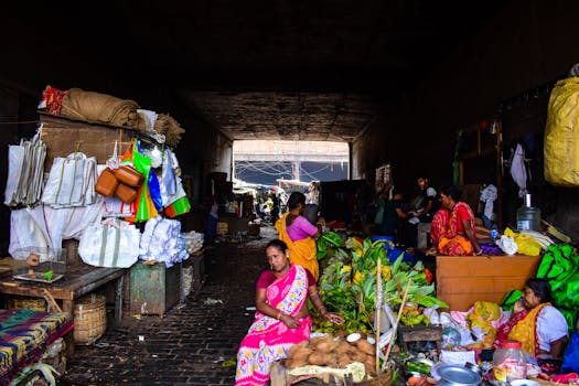 A bustling Indian market scene with women in colorful sarees surrounded by vibrant fabrics and fresh produce.