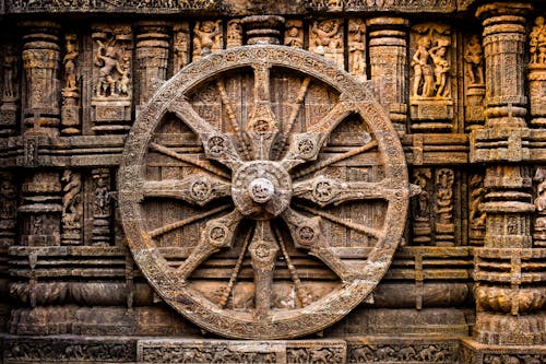 A large wheel is sitting in front of a stone wall
