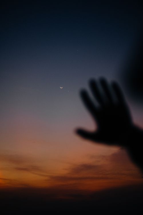 Free A mystical silhouette of a hand reaching towards a crescent moon and stars in a vibrant dusk sky. Stock Photo
