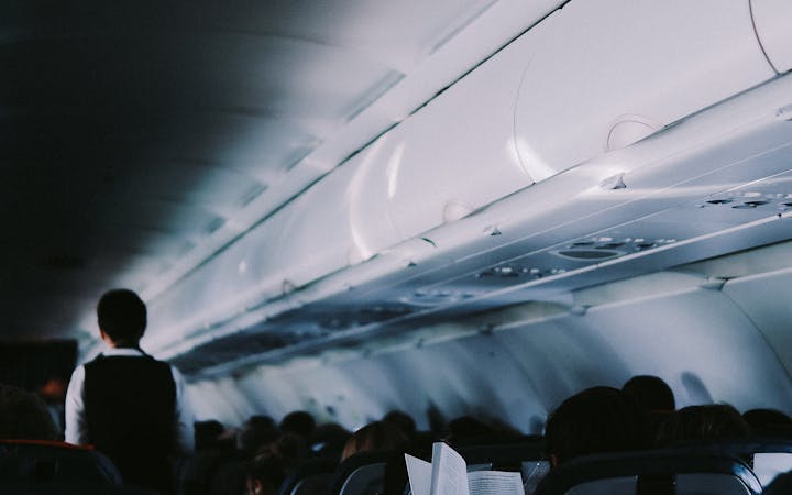 Interior view of airplane cabin with passengers seated and flight attendant in aisle.