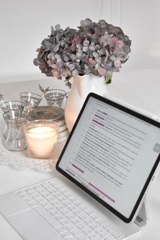 A serene office desk setup with a laptop, burning candle, and vase of flowers for a calming work environment.