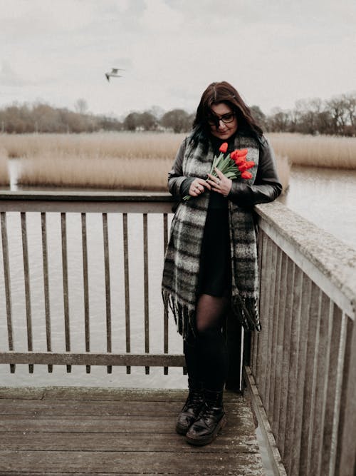 Young Woman Wearing a Scarf, Standing on a Pier with a Bouquet of Tulips 