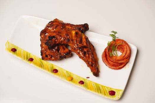 Tantalizing grilled chicken wings served with onion rings, garnished artfully on a designer plate.