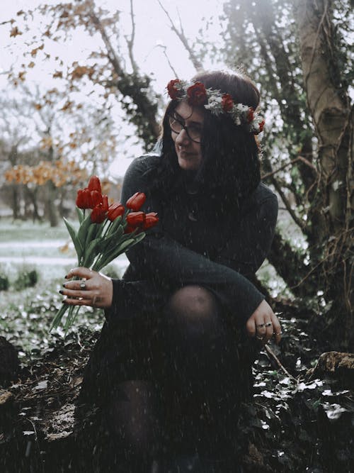 A woman sitting in the snow holding a bunch of tulips