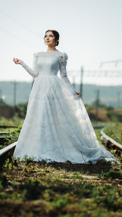 Free A bride in a lace wedding dress stands gracefully on railway tracks in a serene rural setting. Stock Photo