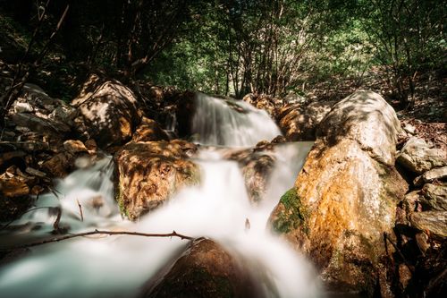 Free A serene waterfall cascades over rocks in a lush forest setting, captured in daylight. Stock Photo
