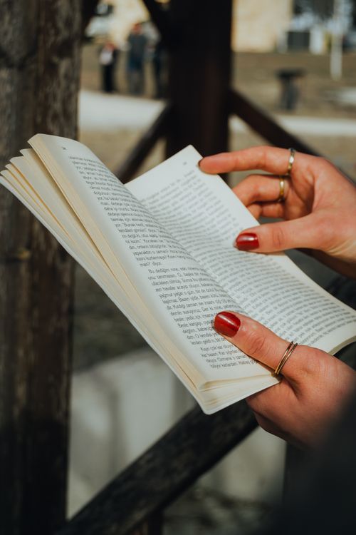 Free A close-up view of a woman's hands with red manicure holding a book outdoors. Stock Photo