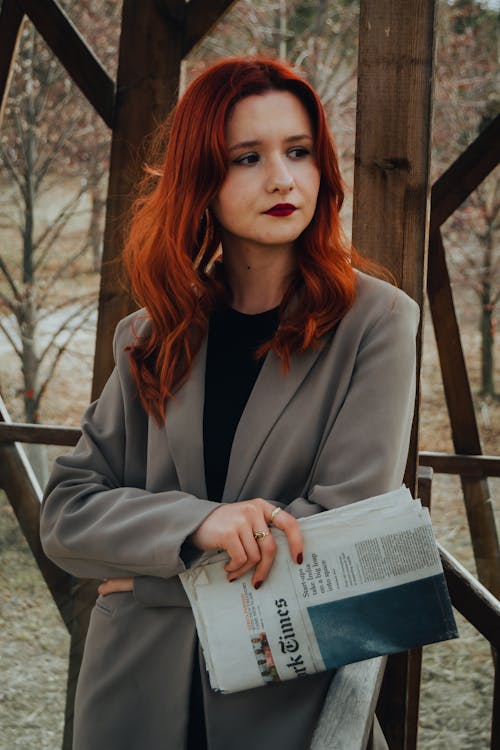 A woman with red hair and glasses holding a newspaper