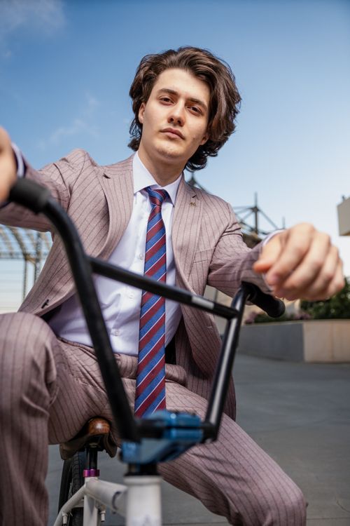 Free A fashionable young man in a suit rides a BMX bike in a modern cityscape. Stock Photo