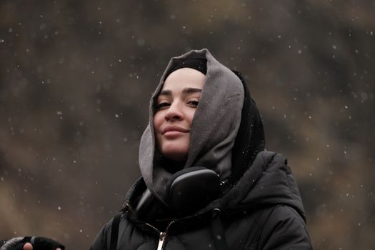 Woman in winter attire smiling amidst a gentle snowfall. Outdoor portrait capturing winter vibes.