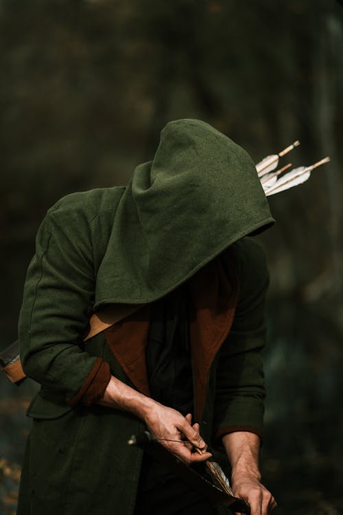 Man Wearing a Hood, Holding a Bow and Arrows in a Forest