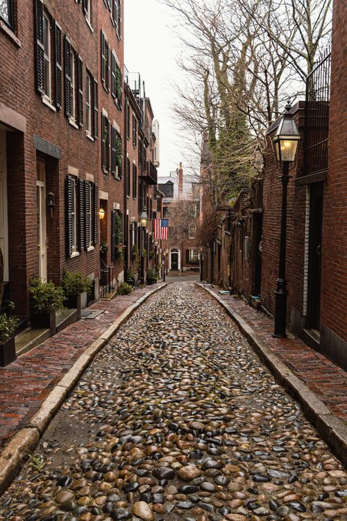 Free Narrow cobblestone street lined with brick buildings and American flag in historic urban locale. Stock Photo