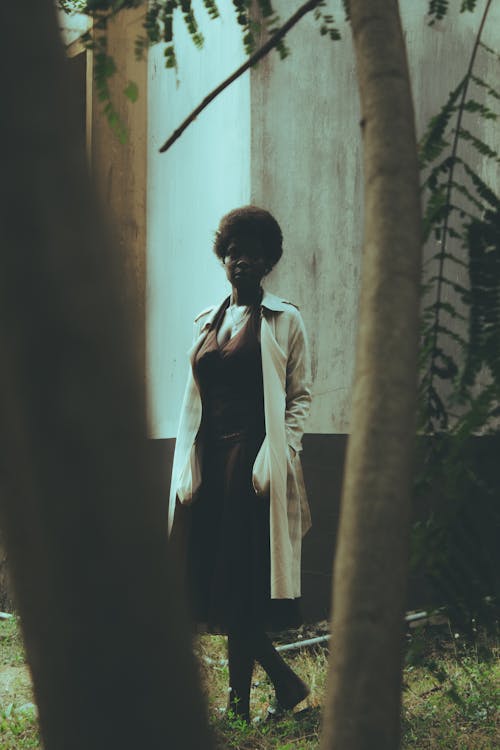 A woman in a trench coat stands in the woods