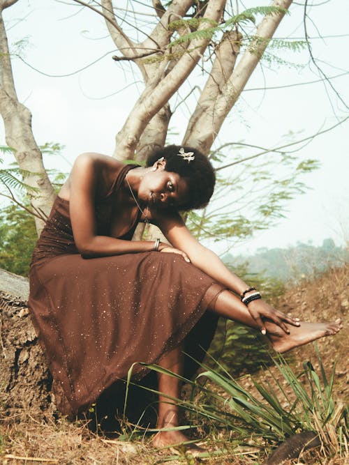 A woman in a brown dress sitting on a tree