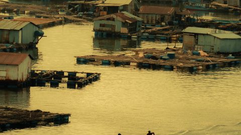 Serene village with stilt houses and boats on a tranquil waterway at sunset.
