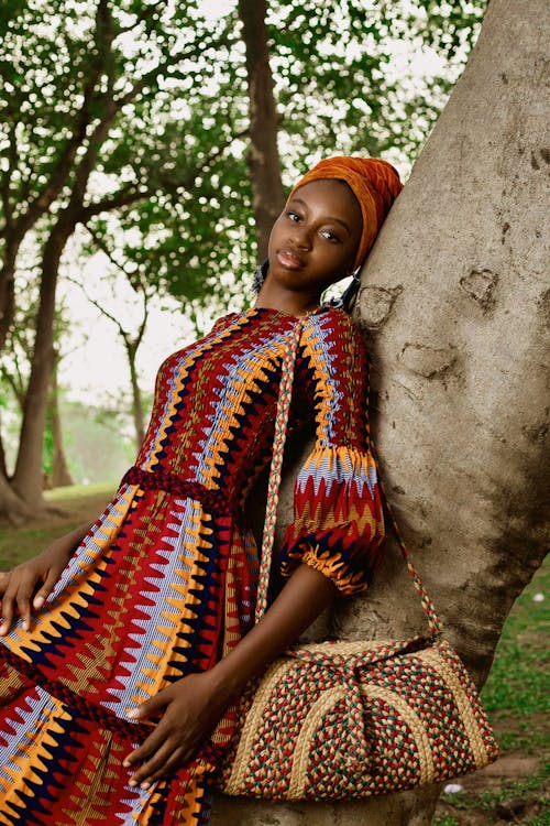 A woman in african dress leaning against a tree
