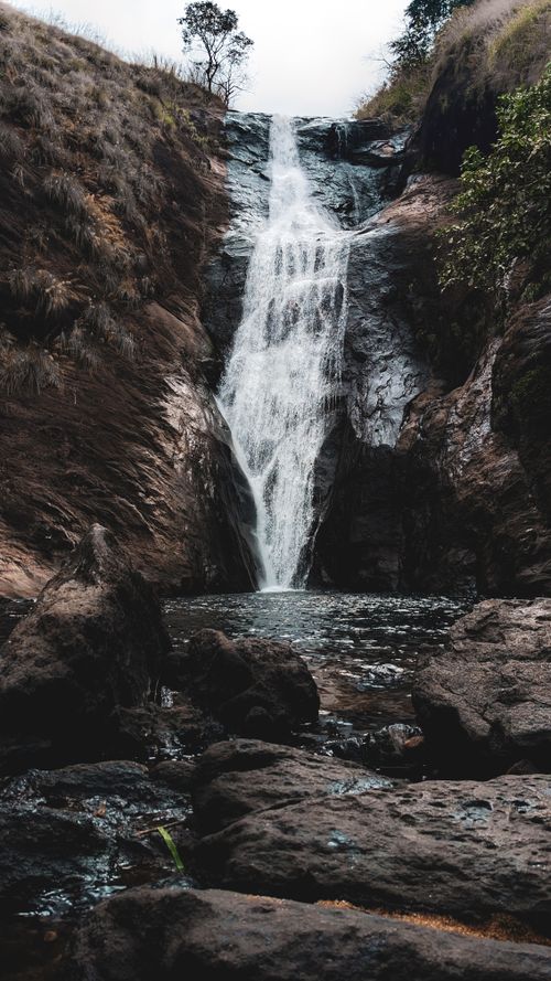 Free Capture of a vertical waterfall cascading down rocky terrain, surrounded by nature. Stock Photo