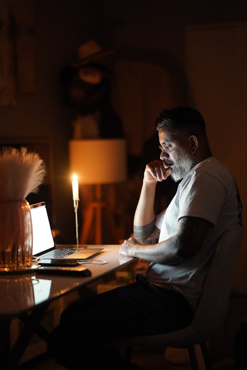 A man sitting at a desk with a laptop and candle