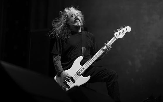 Dynamic black and white photo of an adult male musician with long hair playing a bass guitar passionately.