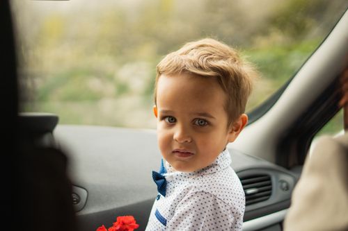 Free Adorable boy in a car holding a flower, dressed in a polka dot shirt with a bowtie. Stock Photo