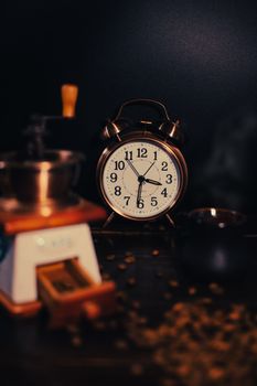 A vintage alarm clock surrounded by coffee beans and a grinder in warm lighting.
