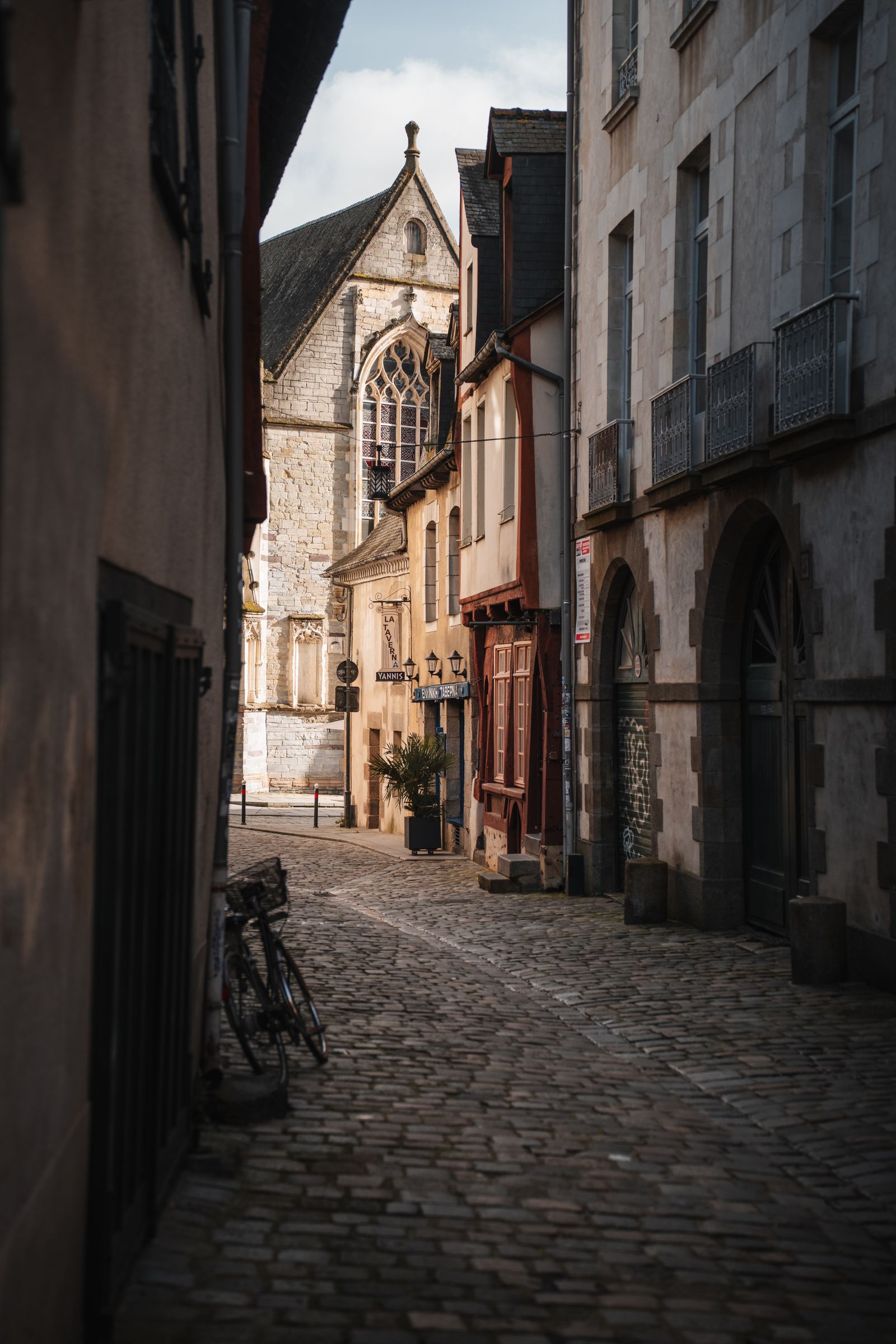 Rue à pans de bois du centre de Rennes au petit matin, pavés humides, rideau de commerce à moitié relevé