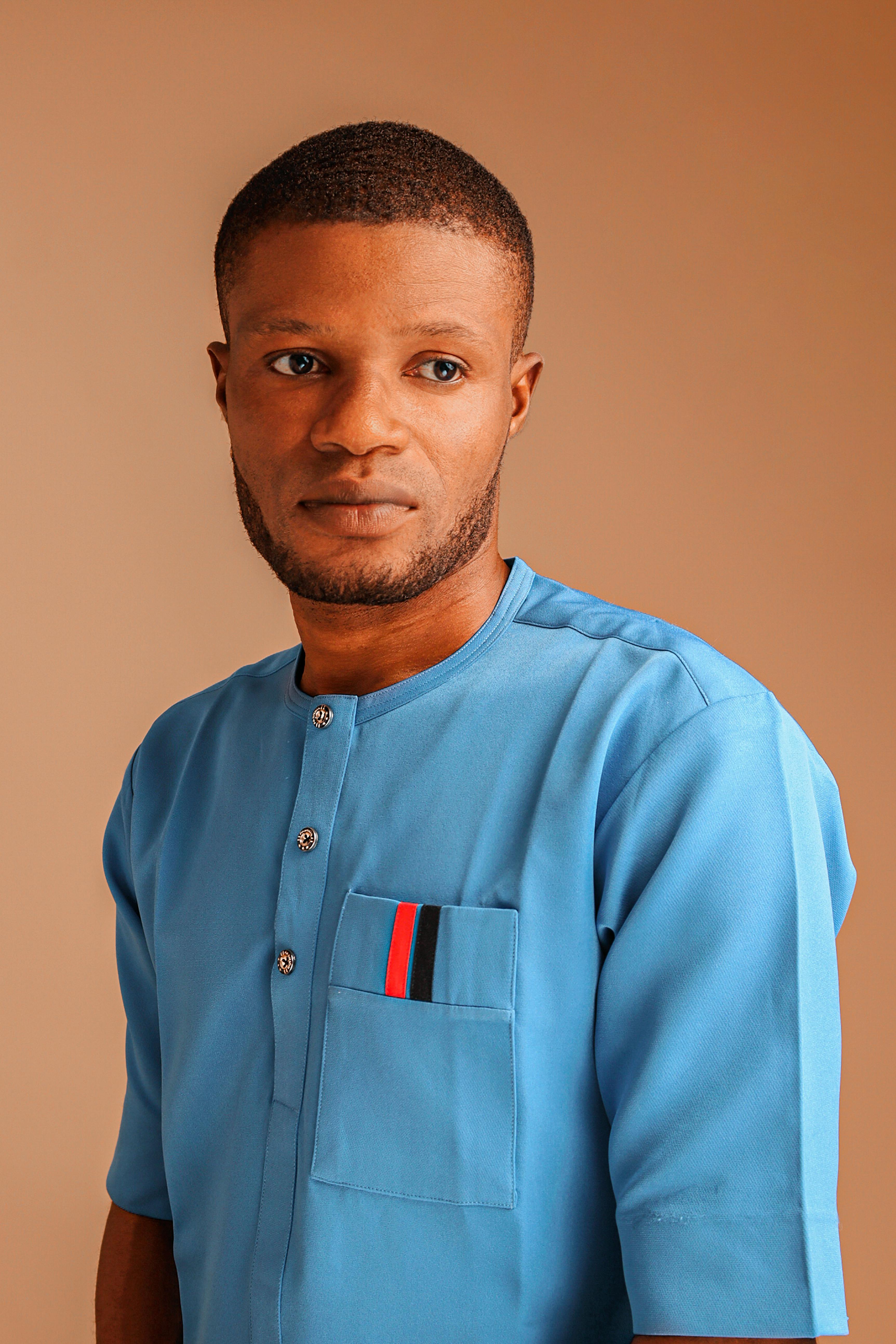 Studio portrait of a man in blue shirt against a brown backdrop, showcasing fashion and style.