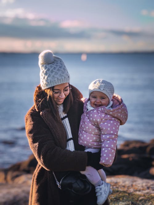 Free A woman holding a baby and standing on a rock by the ocean Stock Photo