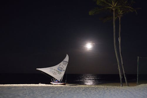 A sailboat on the beach at night with the moon in the sky