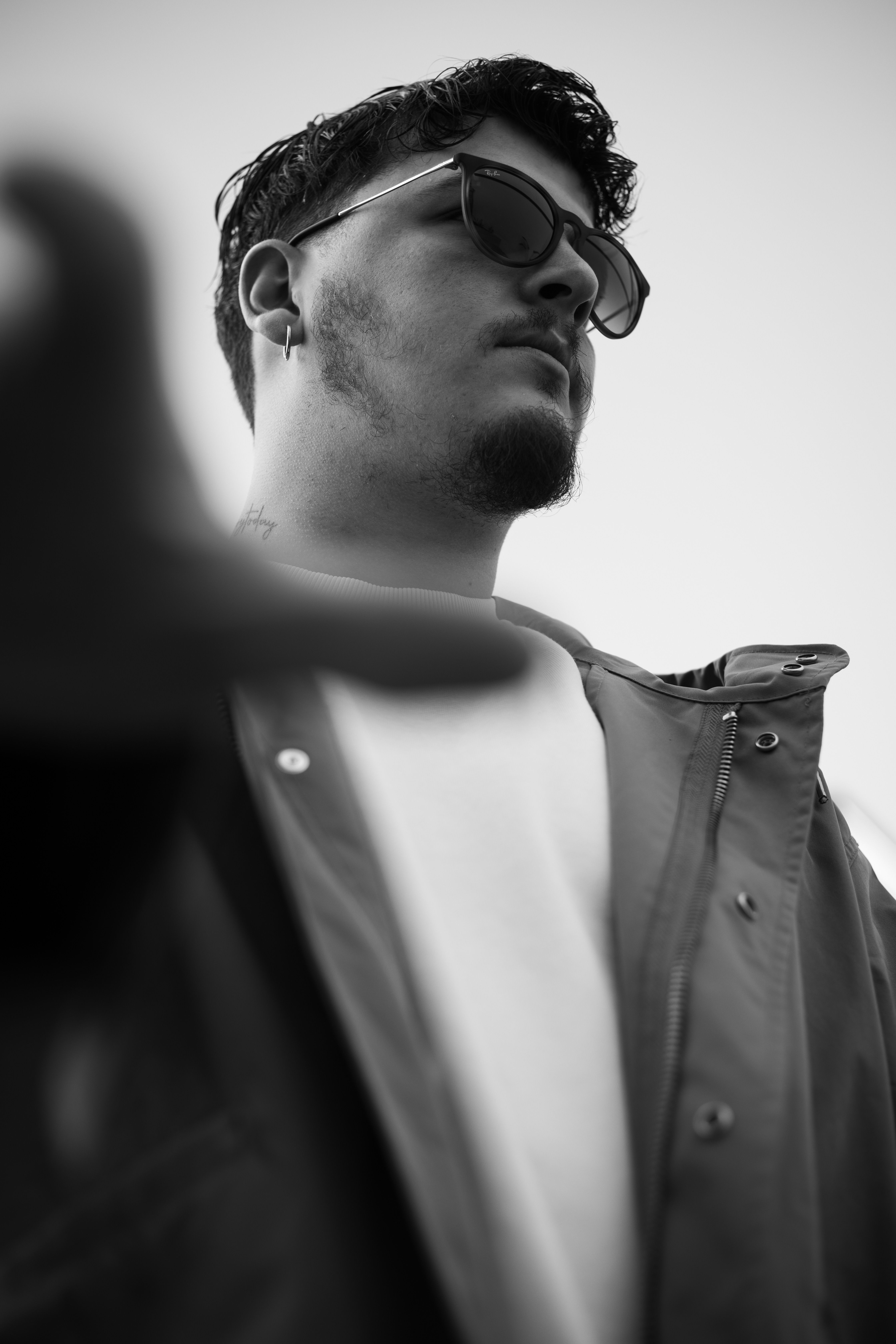 Low-angle black and white portrait of a fashionable man wearing a jacket and sunglasses.