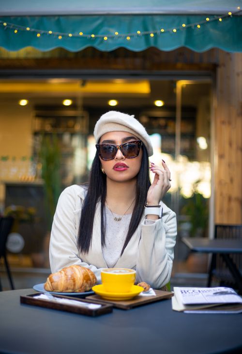 Free Fashionable woman with beret and sunglasses enjoying a croissant and coffee at an outdoor café. Stock Photo