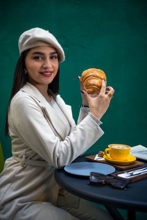 Free Stylish woman in beret with croissant and coffee on a green backdrop, smiling. Stock Photo
